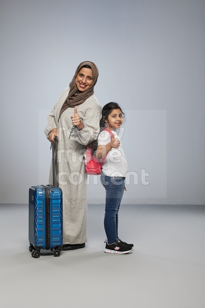 Mom and daughter standing pulling a carry-on bag on gray background