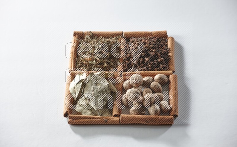 4 squares of cinnamon sticks full of bay laurel leaves, dried basil, cloves and nutmegs on white flooring