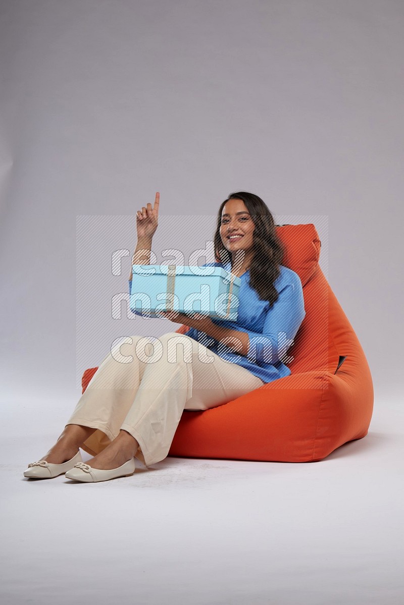 A woman sitting on an orange beanbag and opining a gift