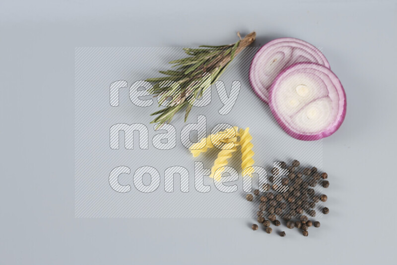 Raw pasta with different ingredients such as cherry tomatoes, garlic, onions, red chilis, black pepper, white pepper, bay laurel leaves, rosemary, cardamom and mushrooms on light blue background
