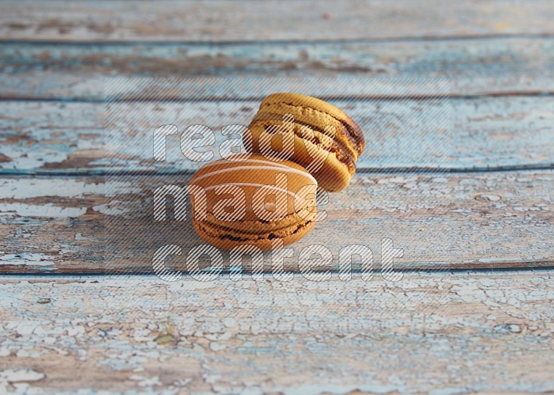 45º Shot of of two assorted Brown Irish Cream, and Yellow Crème Brulée macarons on light blue background