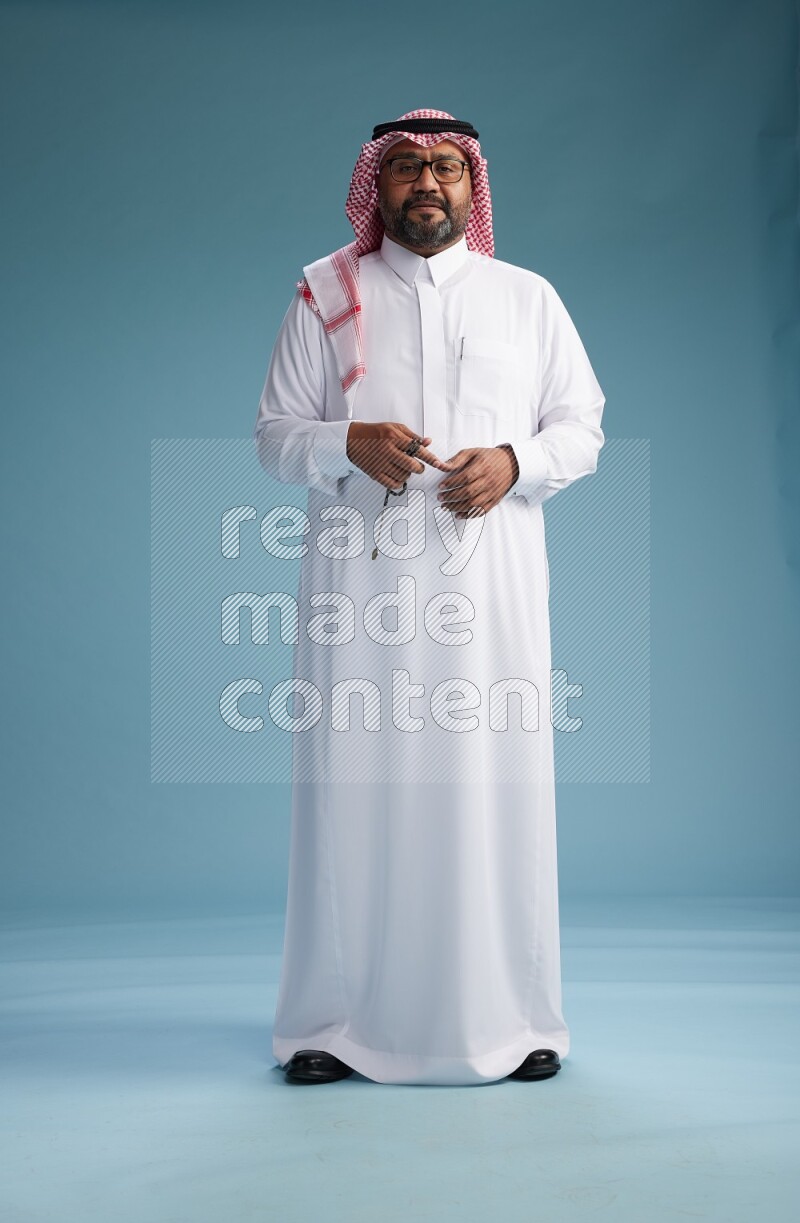 Saudi Man with shimag Standing Interacting with the camera on blue background