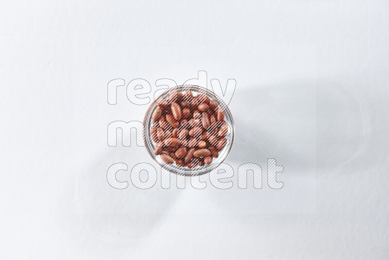 A glass bowl full of red skin peanuts on a white background in different angles