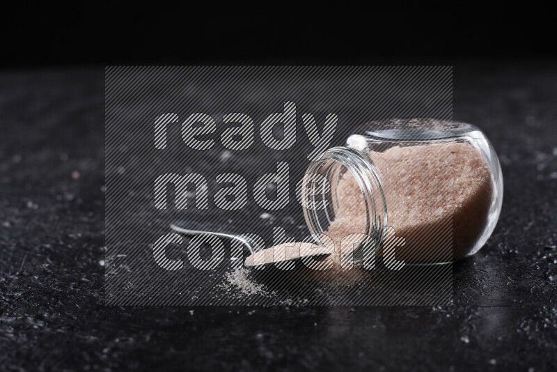 A glass jar full of fine himalayan salt on black background