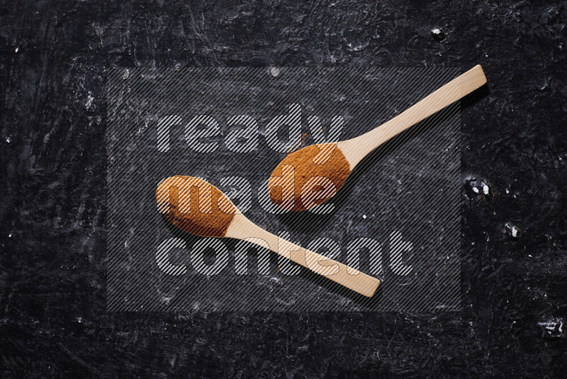 Two wooden spoons full of ground paprika powder on black background