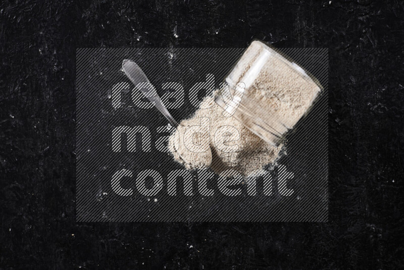 A glass jar full of onion powder flipped with some spilling powder on black background