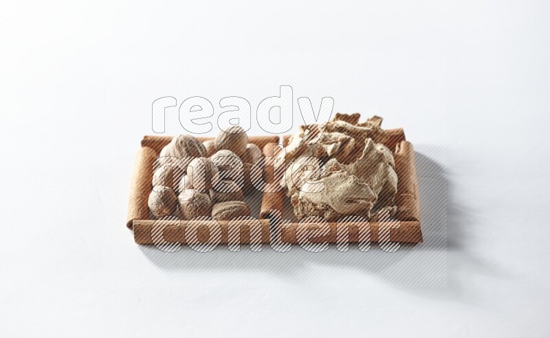 2 squares of cinnamon sticks full of dried ginger and nutmegs on white flooring