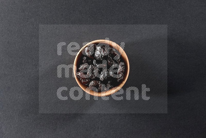 A wooden bowl full of dried plums on a black background in different angles