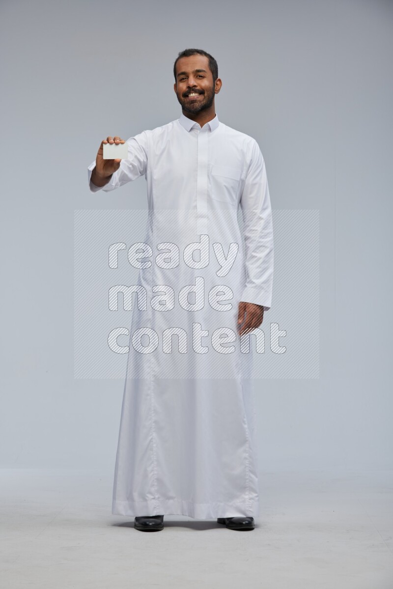 Saudi man wearing Thob standing holding ATM card on Gray background