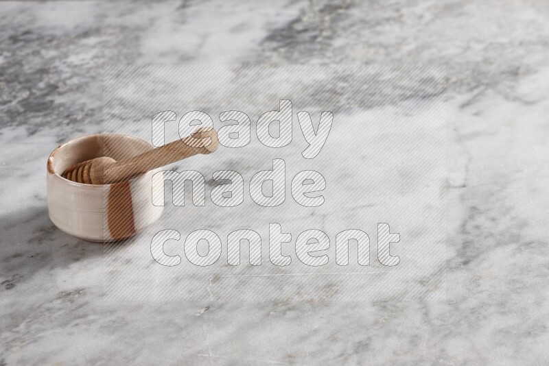 Multicolored pottery bowl with wooden honey dipper in it on grey marble background