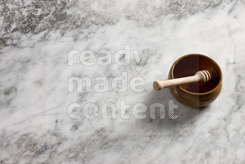 Multicolored Pottery bowl with wooden honey handle in it, on grey marble flooring, 65 degree angle