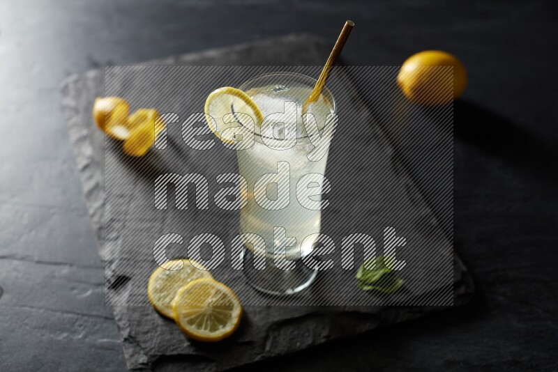 A glass of lemon juice with a straw on black background