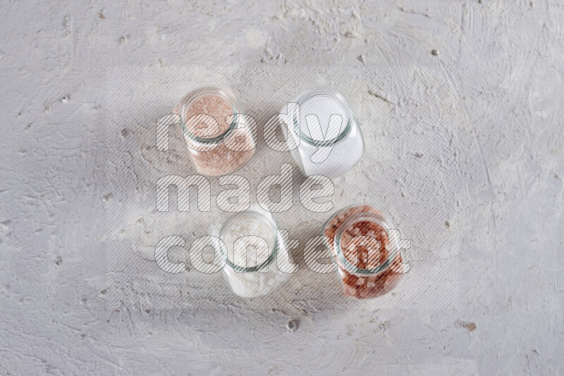 4 glass jars filled with table salt, coarse sea salt, fine himalayan salt and coarse himalayan salt on white background