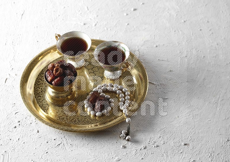 Dates in a metal bowl with tea and prayer beads on a tray in a light setup