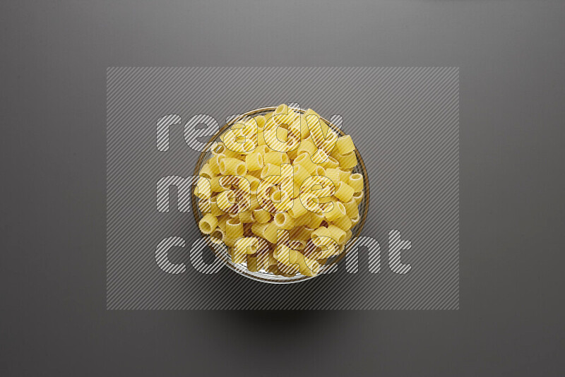 Big rings pasta in a glass bowl on grey background