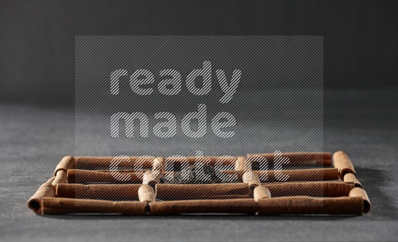 9 مربعات من أعواد القرفة ممتلئة بالشاي في المنتصف محاطة بجوزة الطيب والنعناع المجفف والقرنفل والريحان المجفف والزنجبيل المجفف والقرفة واليانسون والهيل على أرضية سوداء