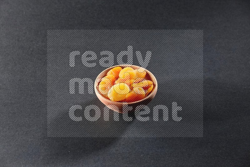 A wooden bowl full of dried apricots on a black background in different angles
