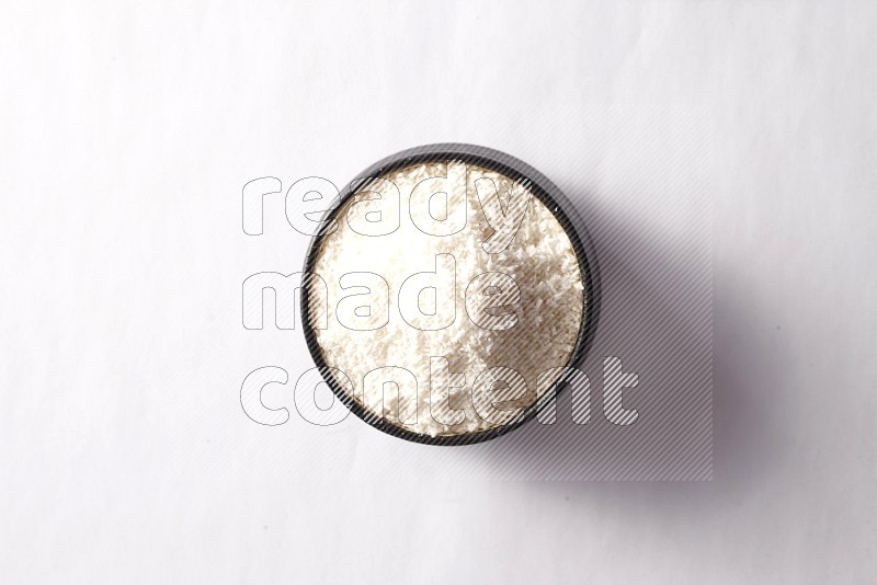 Desiccated coconuts in a black pottery bowl on white background