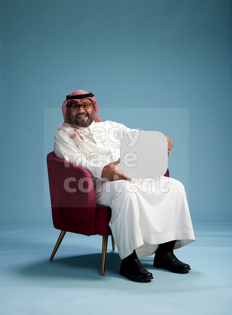 Saudi Man with shimag sitting on chair holding social media sign on blue background
