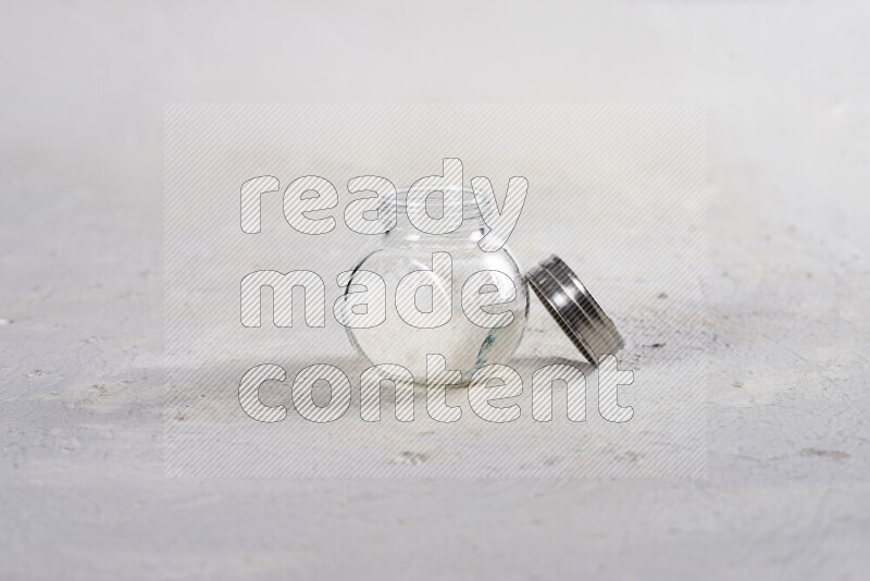 A glass jar full of coarse sea salt crystals on white background