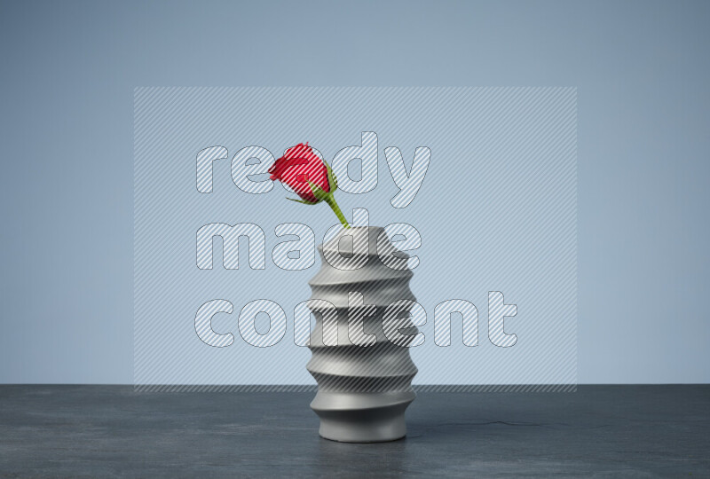 An arrangement of vivid red roses in a grey spiral vase on black marble background