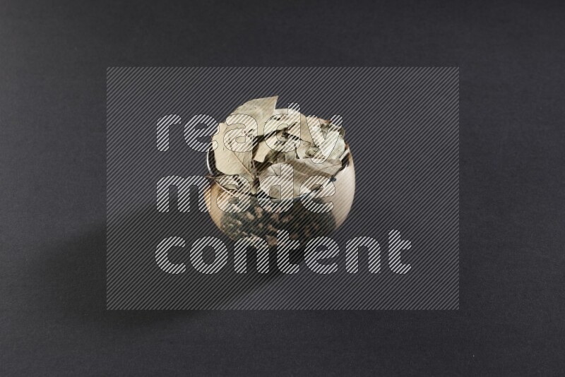 وعاء فخاري متعدد الألوان ممتلئ بأوراق الغار المجففة على أرضية سوداء