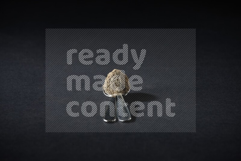 ملعقتان معدنيتان ممتلئتان ببودرة الهيل على خلفية سوداء