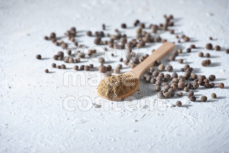 Wooden spoons full of allspice powder and allspice whole balls spreaded on a textured white flooring
