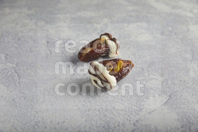 two pistachio stuffed dates covered with white chocolate with dark chocolate drizzle on a light grey background