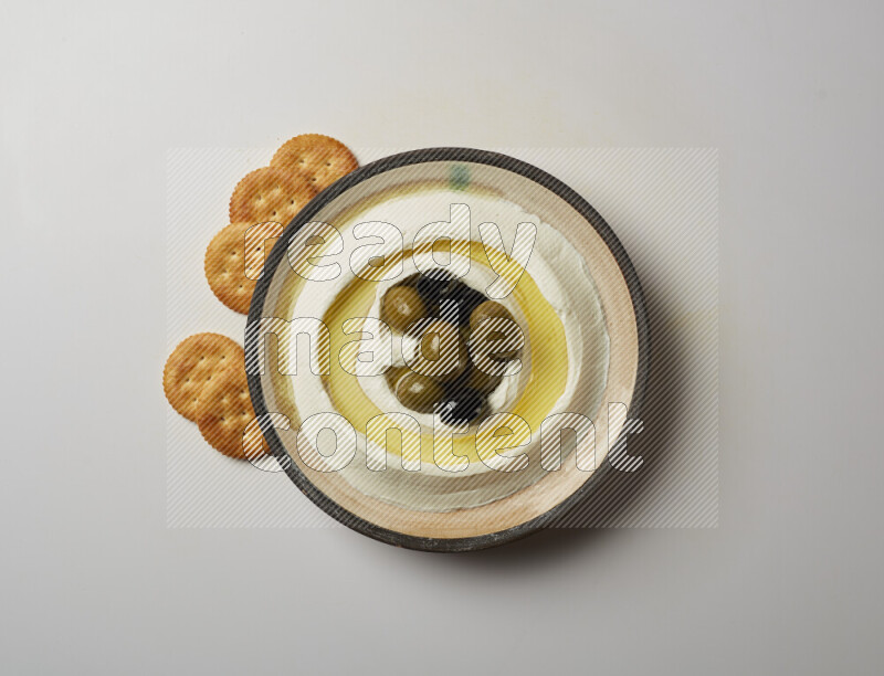 Lebnah garnished with whole black olives in a pottery plate on a white background