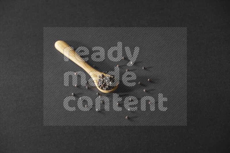 حبوب الفلفل الأسود في ملعقة خشبية علي خلفية سوداء