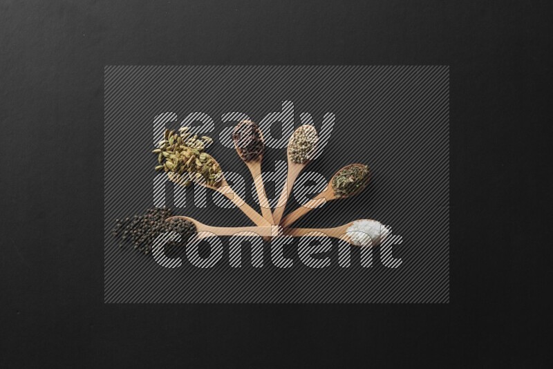 الفلفل الأبيض والقرنفل والهيل والملح والفلفل الأسود وريحان مجفف في معالق خشبية علي خلفية سوداء