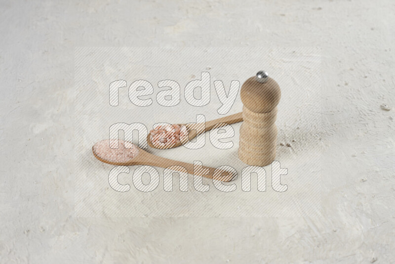 2 wooden spoons filled with fine and coarse salt with wooden grinder beside them on white background