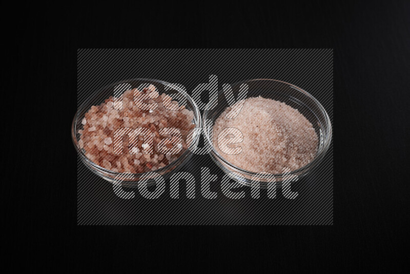 2 glass bowls one is filled with fine himalayan salt and the other with coarse himalayan salt on black background