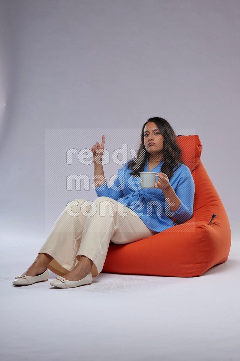 A woman sitting on an orange beanbag and drinking coffee