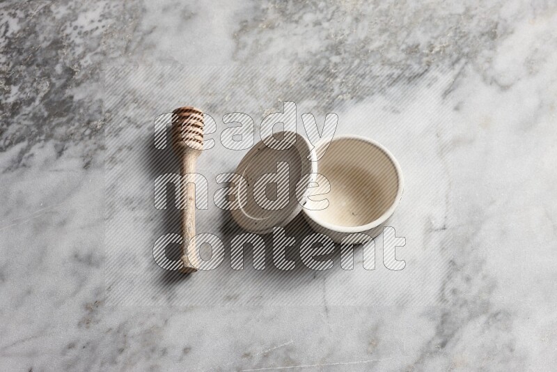 White pottery bowl with wooden honey dipper on the side on grey marble background