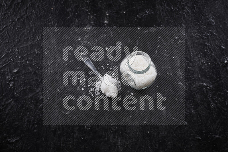 وعاء زجاجي ممتلئ بملح البحر الخشن على خلفية سوداء