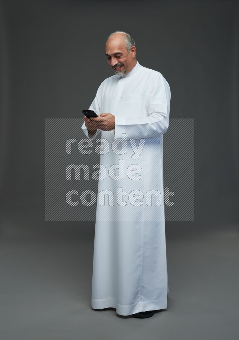 Saudi man without shomag Standing texting on phone on gray background