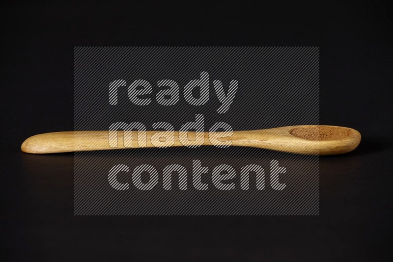 Cinnamon powder in a wooden spoon on a black background