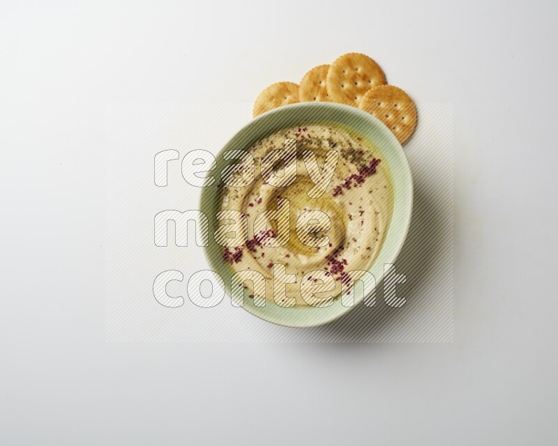 Hummus in a green plate garnished with zattar & sumak on a white background