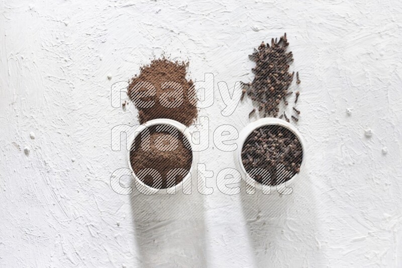 2 Beige ceramic bowls, one full of cloves and the other full of powder on textured white flooring