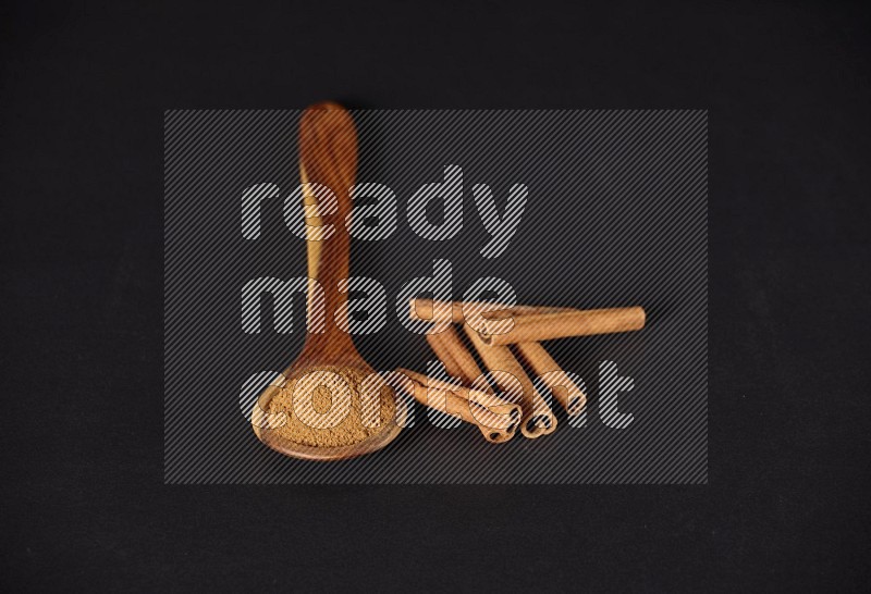 Cinnamon powder in a wooden ladle spoon beside it cinnamon sticks on the flooring on black background in different angles