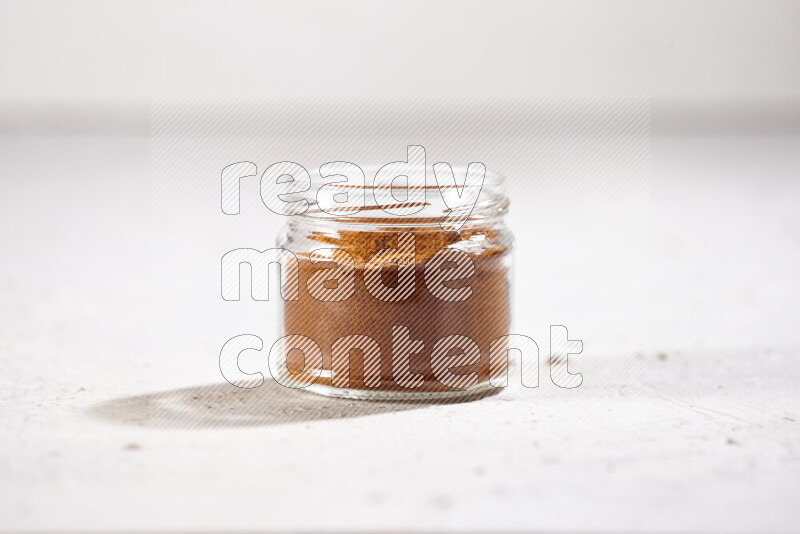 A glass jar full of ground paprika powder on white background