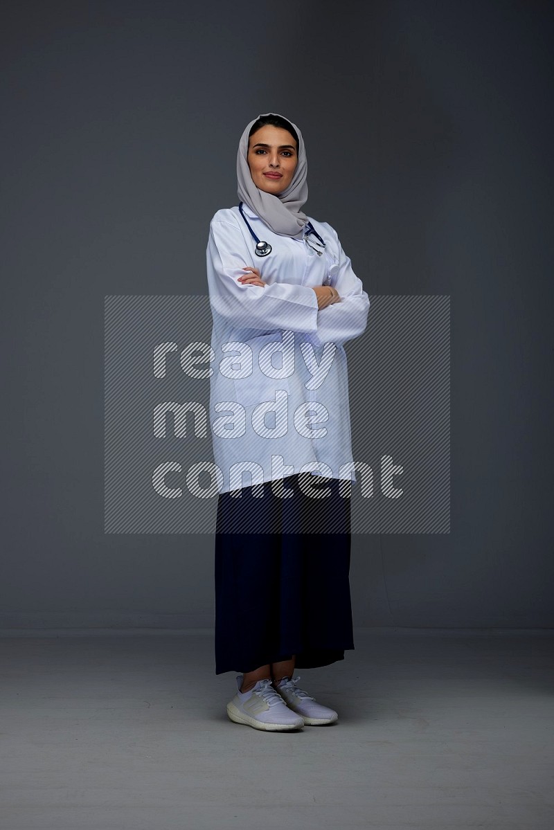 A female doctor wearing a light gray head scarf standing on grey background.