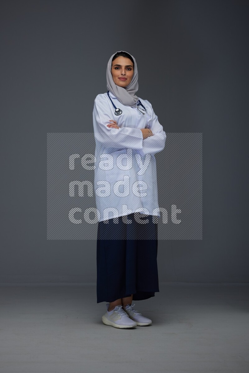 A female doctor wearing a light gray head scarf standing on grey background.