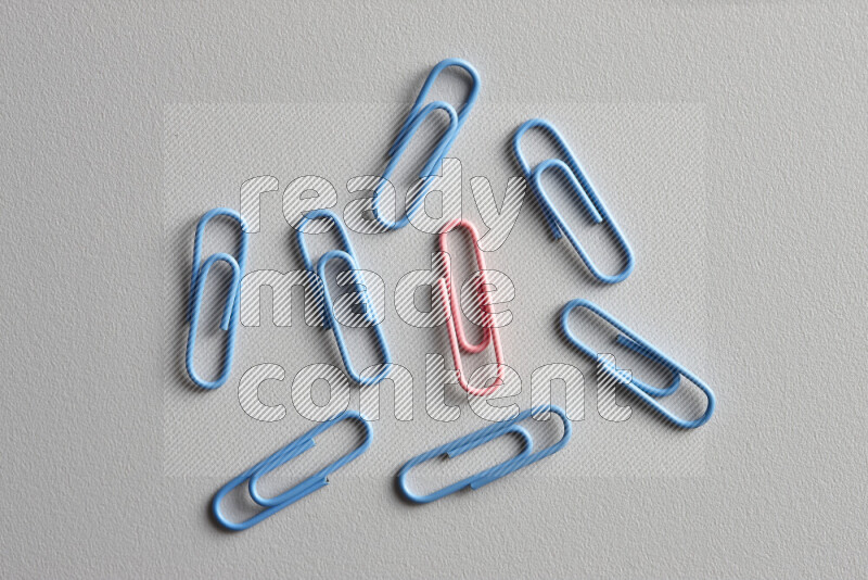A pink paperclip surrounded by bunch of blue paperclips on grey background