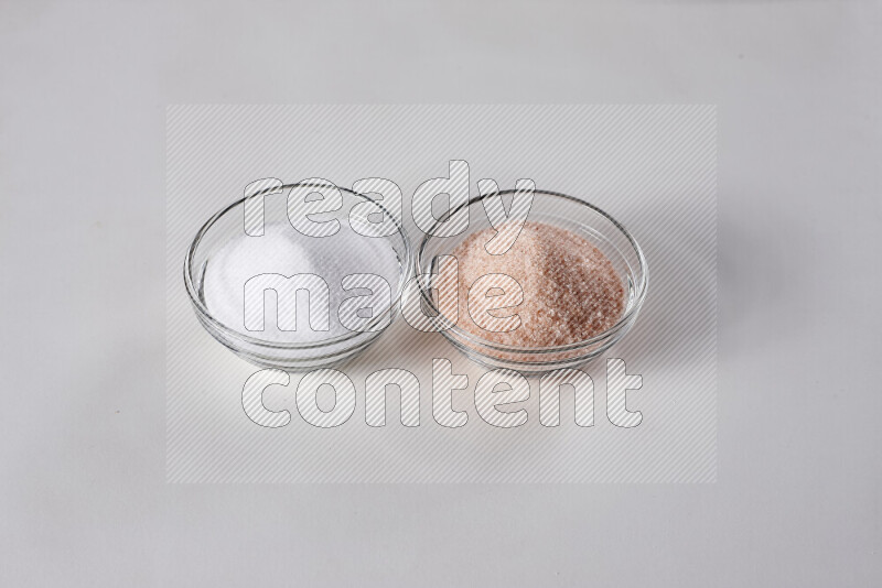 2 glass bowls one is filled with himalayan salt and the other with white salt on white background