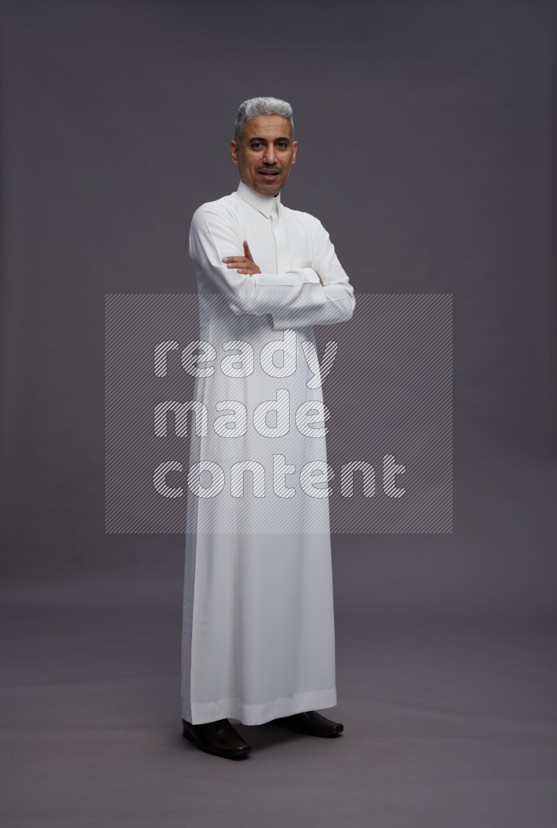 Saudi man wearing thob standing with crossed arms on gray background