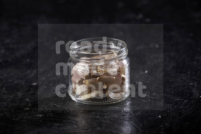 A glass jar full of garlic cloves on a textured black flooring in different angles