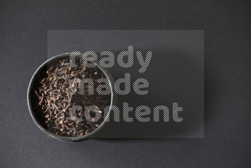 وعاء فخاري أسود ممتلئ بحبوب القرنفل علي خلفية سوداء